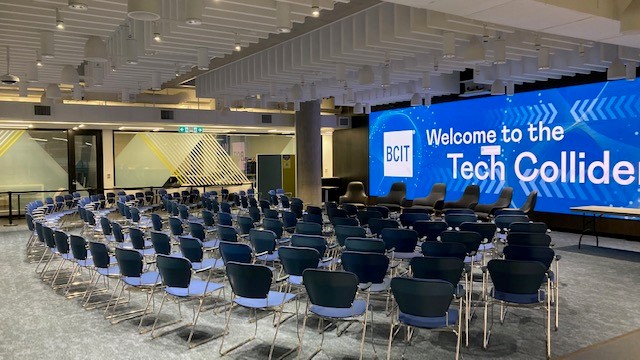Image of the Tech Collider event space - a large wall screen saying welcome to the Tech Collider with seating in front.